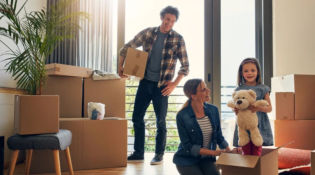 A family joyfully moving into a new home, surrounded by boxes, symbolizing new beginnings and stability.