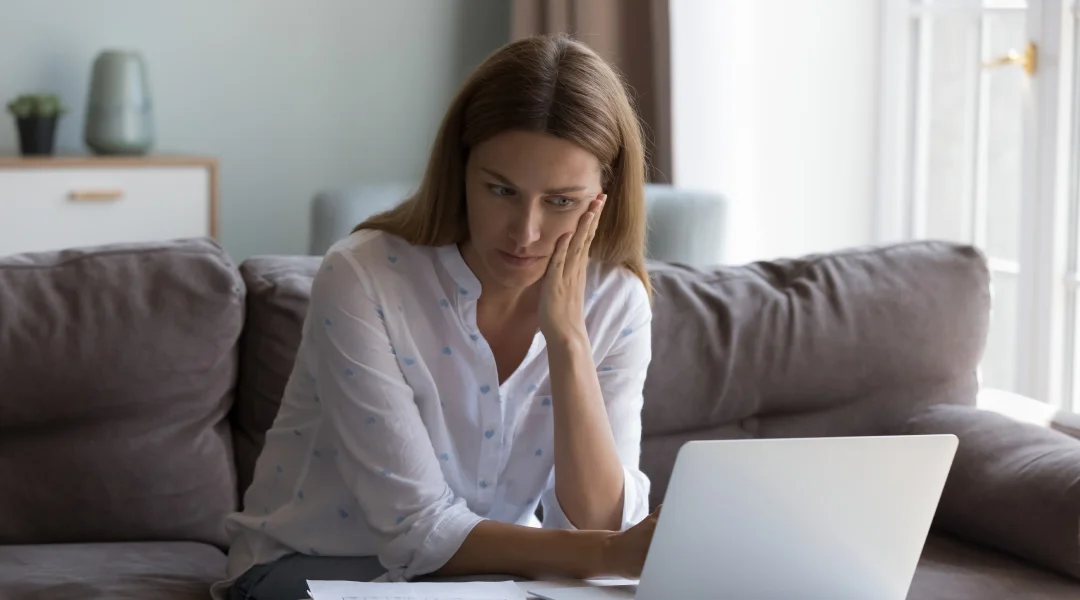 A woman on a couch using a laptop, possibly researching options for payday loans.