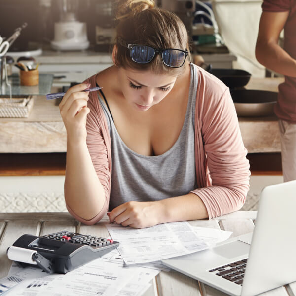 Une femme assise à une table, utilisant un ordinateur portable, entourée de documents sur la consolidation de dettes.