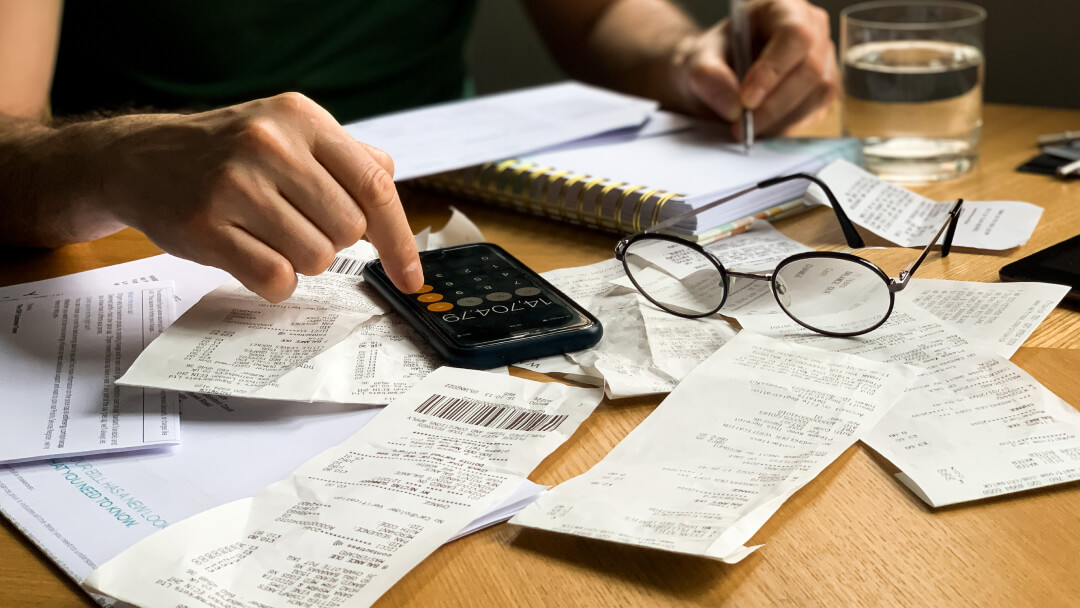 Homme avec des lunettes, calculatrice sur la table, entouré de reçus et de papiers, en train de travailler sur ses finances.