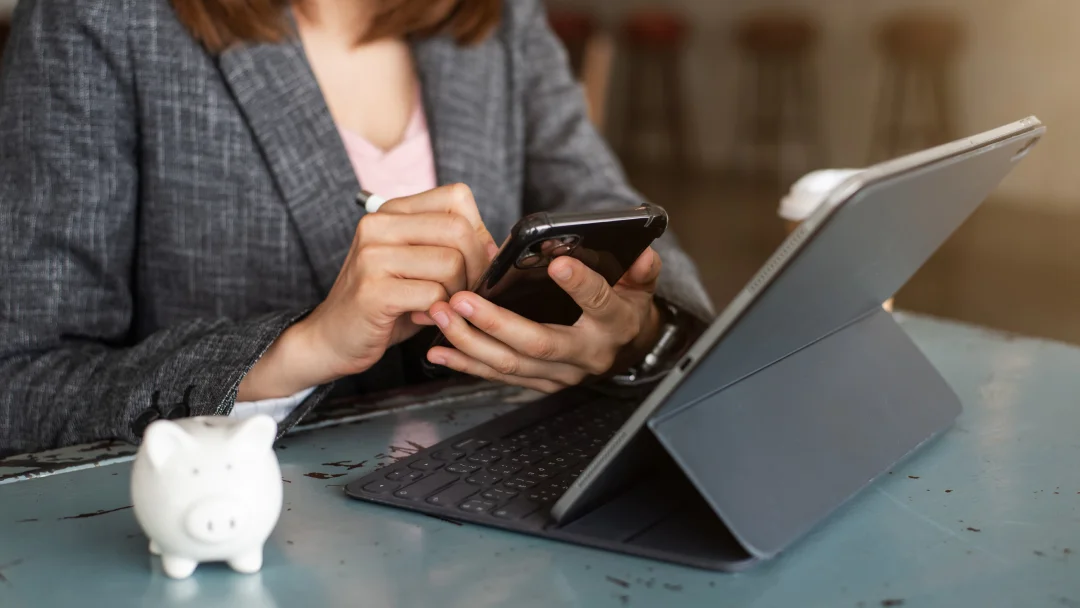 Businesswoman at a cafe, using a smartphone and tablet to research the best personal loan options.