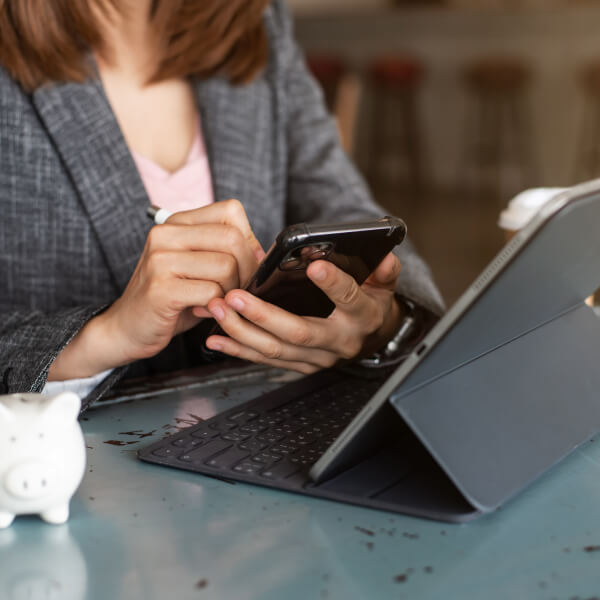 A woman in a business suit uses her phone, sitting at a table with a piggy bank, illustrating digital loans in 2026.